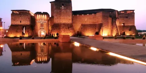 Castello Sismondo illuminato di sera, con riflessi sull'acqua. Un luogo che evoca la magia del cinema, come un museo felliniano a Rimini.