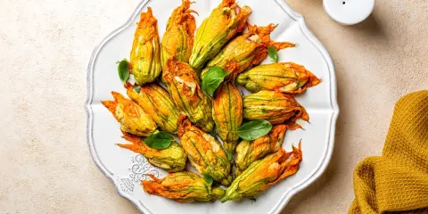 Fiori di zucca al forno ripieni, dorati e invitanti, disposti su un piatto bianco, con foglie di basilico fresco.