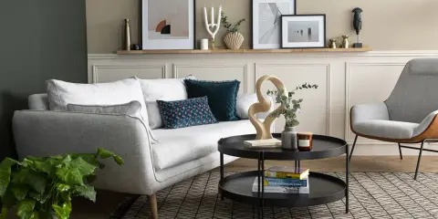 Salon moderne avec canapé gris clair, coussins décoratifs et une sculpture abstraite. La décoration murale au-dessus du canapé complète l'ensemble.