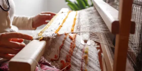Hands weave a textured fabric on a loom, a beautiful example of textile upcycling.