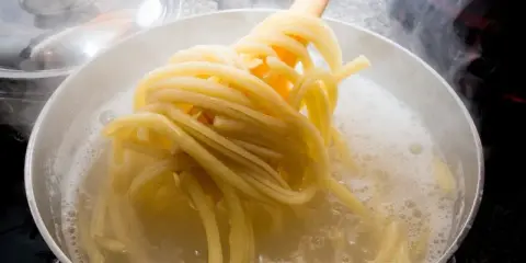 Gorący garnek z bulgoczącą wodą, z którego wyciągane są idealne, sprężyste nitki makaronu al dente.