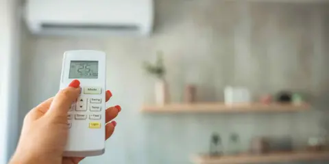 Mano con control remoto ajustando la temperatura ideal aire acondicionado para dormir a 25°C.