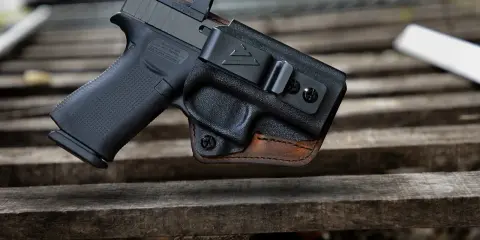 Pistolet w kaburze udowej z czarnego polimeru i brązowej skóry, z widocznym celownikiem optycznym.