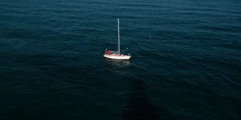 Un voilier blanc et rouge est au mouillage sur une mer sombre. La question est : combien de temps peut on rester au mouillage dans ce décor paisible ?