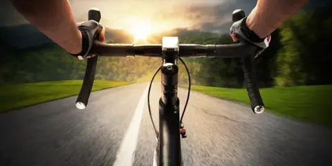 Rowerzysta w rękawiczkach mija pola i lasy, celując w zachód słońca. Dziś na liczniku pojawi się 100 km na rowerze.