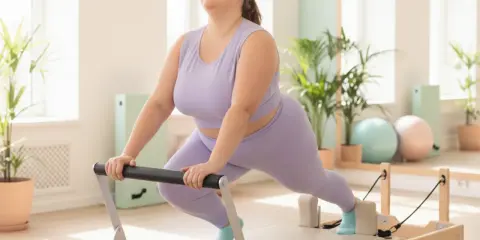 Frau lacht glücklich bei Pilates-Übungen auf einem Reformer. Pilates zum Abnehmen ist eine tolle Möglichkeit, fit zu werden.