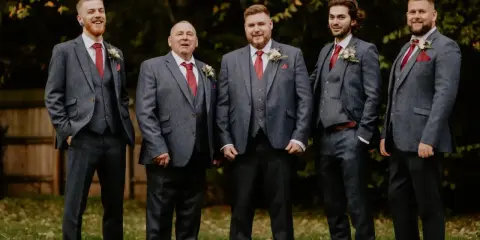 Five men in matching grey suits with red ties and pocket squares. The price of tuxedos can vary, but these look like a good investment for a wedding party.