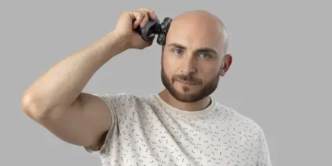 Mężczyzna goli głowę na zero za pomocą golarki.