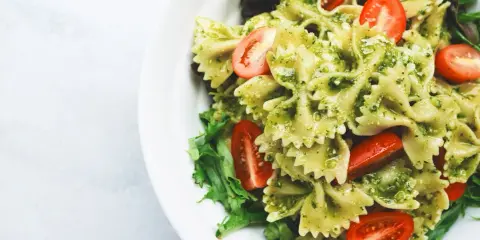 Pyszna sałatka z makaronem farfalle w sosie pesto, z pomidorkami koktajlowymi i świeżą sałatą.
