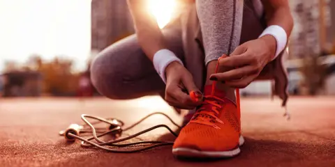 Frau bindet ihre neuen laufschuhe ein. Die Sonne scheint, ein Springseil liegt bereit.