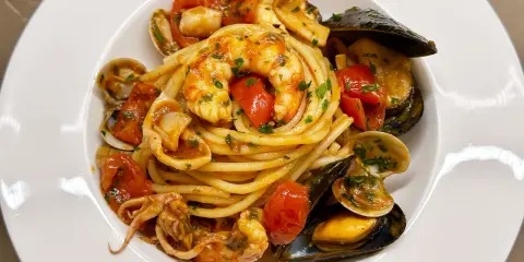 Spaghetti allo scoglio with shrimp, mussels, clams, squid, and cherry tomatoes in a white bowl.
