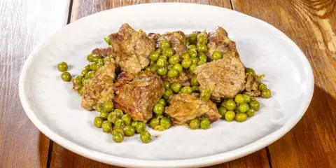 Un saporito agnello con piselli, un classico piatto italiano, servito su un piatto bianco.
