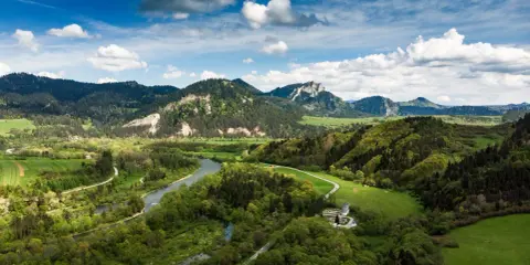 Malownicze **Pieniny** w okolicach **Szczawnicy** z meandrującym Dunajcem, zielonymi łąkami i skalistymi szczytami pod błękitnym niebem.