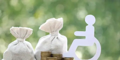 Pieniądze i symbol osoby na wózku inwalidzkim. Zastanawiasz się, ile wynosi świadczenie wspierające?