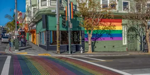 A vibrant rainbow crosswalk leads to a building adorned with a large rainbow mural, a symbol of the gay bed breakfast scene in San Francisco.