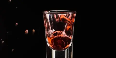 Wściekły pies drink, moneta spada do kieliszka z czerwonym płynem, tworząc fontannę.