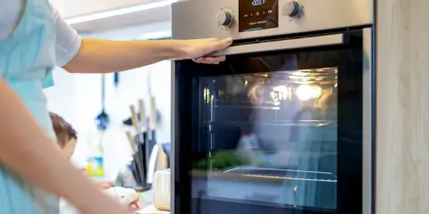 Une main ouvre la porte d'un four moderne. L'ampérage du four est réglé pour une cuisson parfaite.