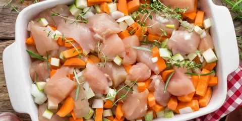 Duszona pierś z kurczaka z warzywami: kawałki kurczaka, marchewki, cukinii i cebuli w naczyniu żaroodpornym, gotowe do pieczenia.