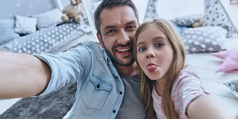 Padre e figlia si scattano un selfie giocoso, un'immagine che cattura la gioia del loro rapporto padre-figlia, quasi come in un'interpretazione freudiana della felicità.