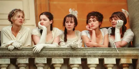 Cinque donne in abiti d'epoca, forse sorelle, riflettono su orgoglio e pregiudizio mentre guardano da un balcone.