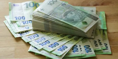 Stos banknotów 100 zł i 100 euro na drewnianym blacie. Może to być kwota na zasiłek stały.