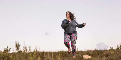 Frau joggt mit Gewichten in bunter Hose durch die Natur.
