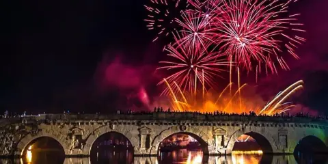 Fuochi d'artificio spettacolari illuminano il cielo notturno sopra un ponte storico, celebrando il capodanno in riviera romagnola.