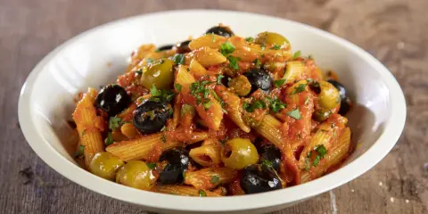 Penne al sugo rosso con olive nere e verdi, capperi e prezzemolo, un piatto di pasta alla puttanesca invitante.