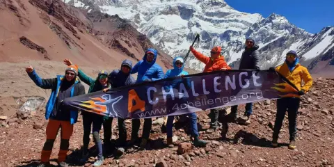Grupa zdobywców z banerem "4 CHALLENGE" na tle majestatycznych gór z Aconcagua.