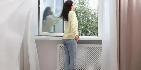 Mujer abre ventana para ventilar la casa en invierno. Reflejo en el cristal muestra a otra persona.