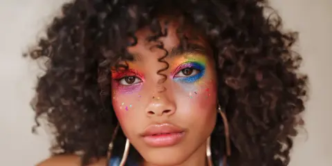 Un rostro con un vibrante maquillaje de ojos arcoíris y purpurina, celebrando la diversidad y el orgullo.
