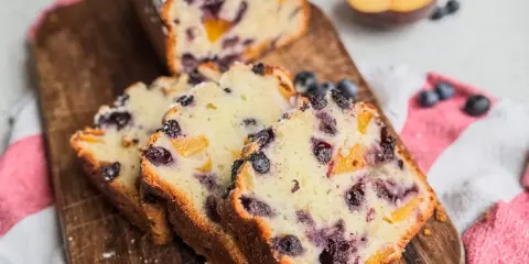 Saftiger Joghurt Kuchen mit Blaubeeren und Pfirsichstücken, bestäubt mit Puderzucker.