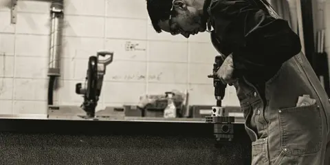 Giovane operatore CNC senza esperienza impara a usare un trapano, concentrato sul lavoro.