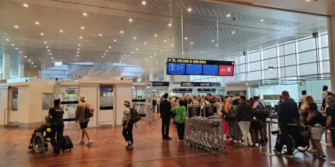 Ludzie w terminalu lotniska, tablice z informacjami o bramkach i pasażerowie z bagażami.