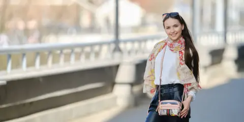 Uśmiechnięta kobieta w kwiecistym szalu i czarnych spodniach na tle mostu.