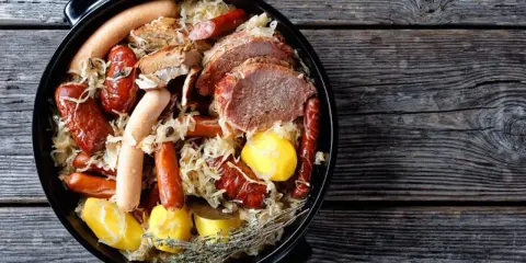 Choucroute garnie, un plat emblématique des alsace spécialités culinaires, avec saucisses, viandes et pommes de terre dans une cocotte.