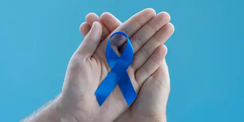 Dłonie trzymające niebieską wstążkę symbolizującą wsparcie dla mężczyzn. Warto poznać domowe sposoby na prostatę.