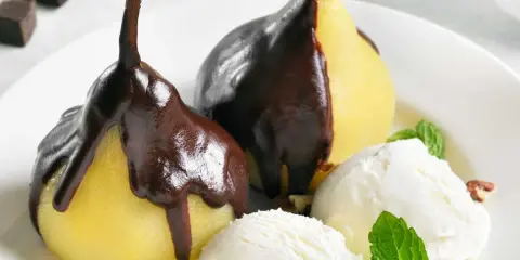 Poires pochées nappées de chocolat noir, servies avec de la glace à la vanille et des éclats de noisettes. Un délice de poire Belle Hélène.