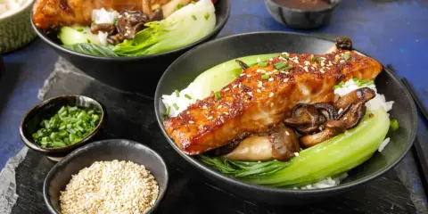 Två skålar med ris, bok choy, svamp och glaserad sous vide lax, toppad med sesamfrön och gräslök.