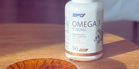 Biała butelka suplementu diety Omega 3 Strong. Na małej, bursztynowej podstawce leży jedna kapsułka. Kwasy omega 3 na co? Na zdrowie!