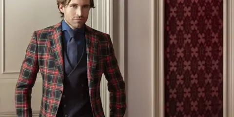 Man in a festive tartan blazer, dark blue shirt, tie, and vest. This is what holiday attire looks like.