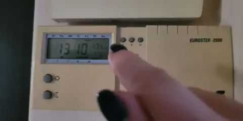 Dłoń z czarnym lakierem na paznokciach dotyka termostatu, sterowanie piecem gazowym. Na wyświetlaczu 13:10 i 17.5°C.