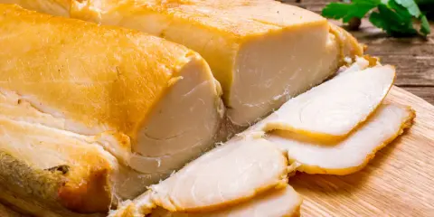 Dwa kawałki wędzonej ryby maślanej, jeden pokrojony w plastry, leżą na desce.