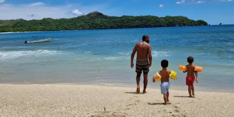 Un padre cammina sulla spiaggia con i suoi due figli, pronti per un'avventura in Costa Rica con bambini.