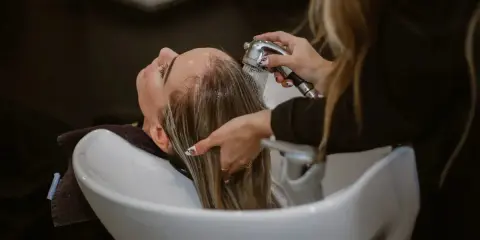 Una parrucchiera sciacqua i capelli di una cliente in un lavatesta, mostrando come lavare i capelli senza shampoo.
