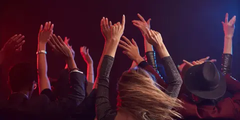 Människor med uppsträckta armar dansar i mörkret, upplysta av rött och blått ljus. En festlig kväll i Stockholm.