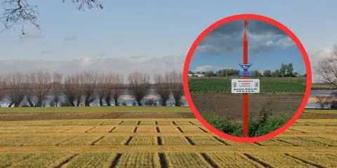Najniższy punkt w Polsce, oznaczony tablicą informującą o poziomie depresji 1,8 m p.p.m., na tle pola i rzeki.