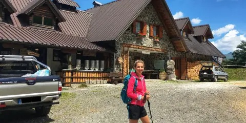 Ragazza con zaino e bastoncini da trekking davanti alla malga Lavareit, con un pick-up e un'auto parcheggiati.