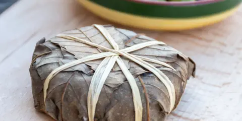 Un mets emballé dans des feuilles séchées, lié par des brins, évoquant les spécialités des Hautes-Alpes.