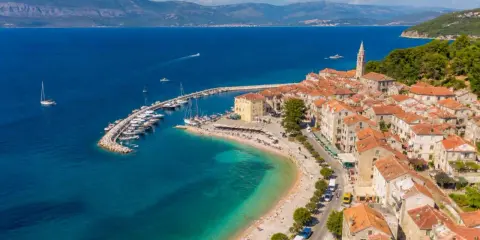 Malownicze miasteczko na wyspie Brač z portem pełnym łodzi, plażą i kamiennymi domami pod czerwonymi dachami.